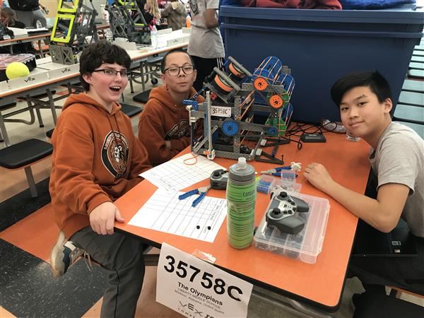 Three students pose with their robot and team number.